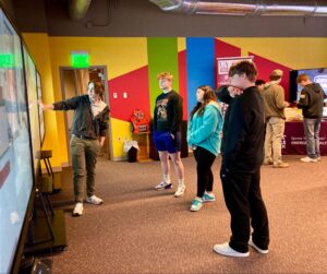 A man is talking to a group of people about a digital hallway being displayed on a computer screen.