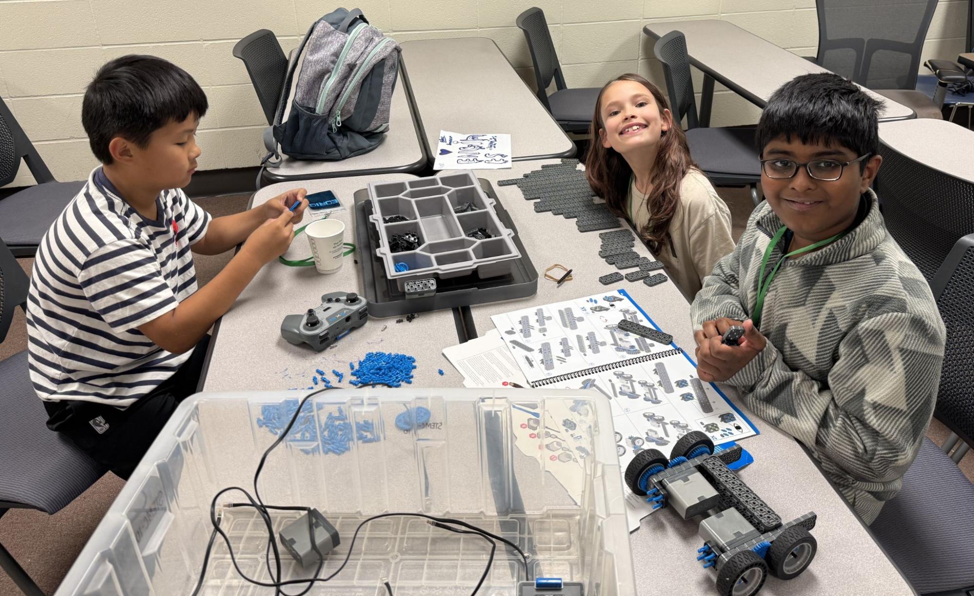 A trio of young campers are working on building a robot together.