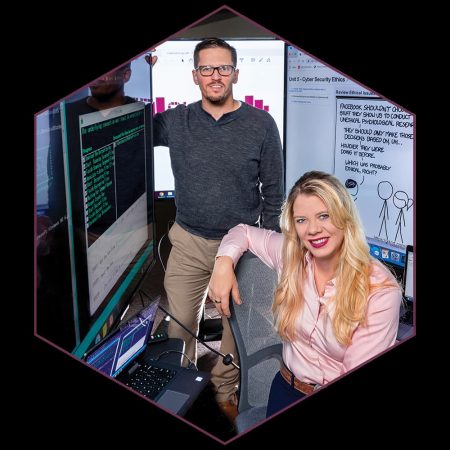 Two cybersecurity professionals in a high-tech workspace with multiple computer screens displaying code, graphs, and cybersecurity concepts.
